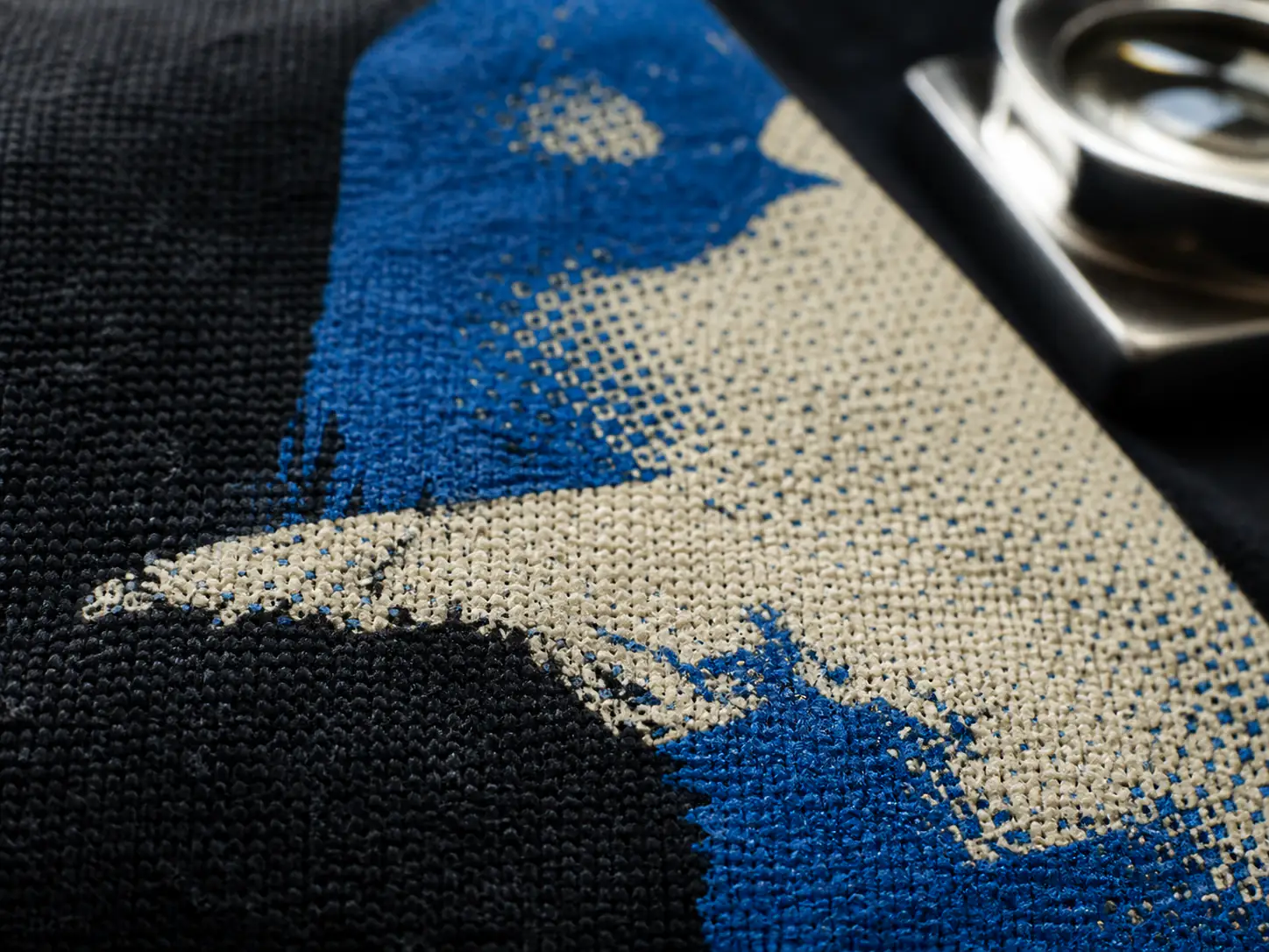 Macro view of cream and cobalt screen-print ink following black cotton texture
