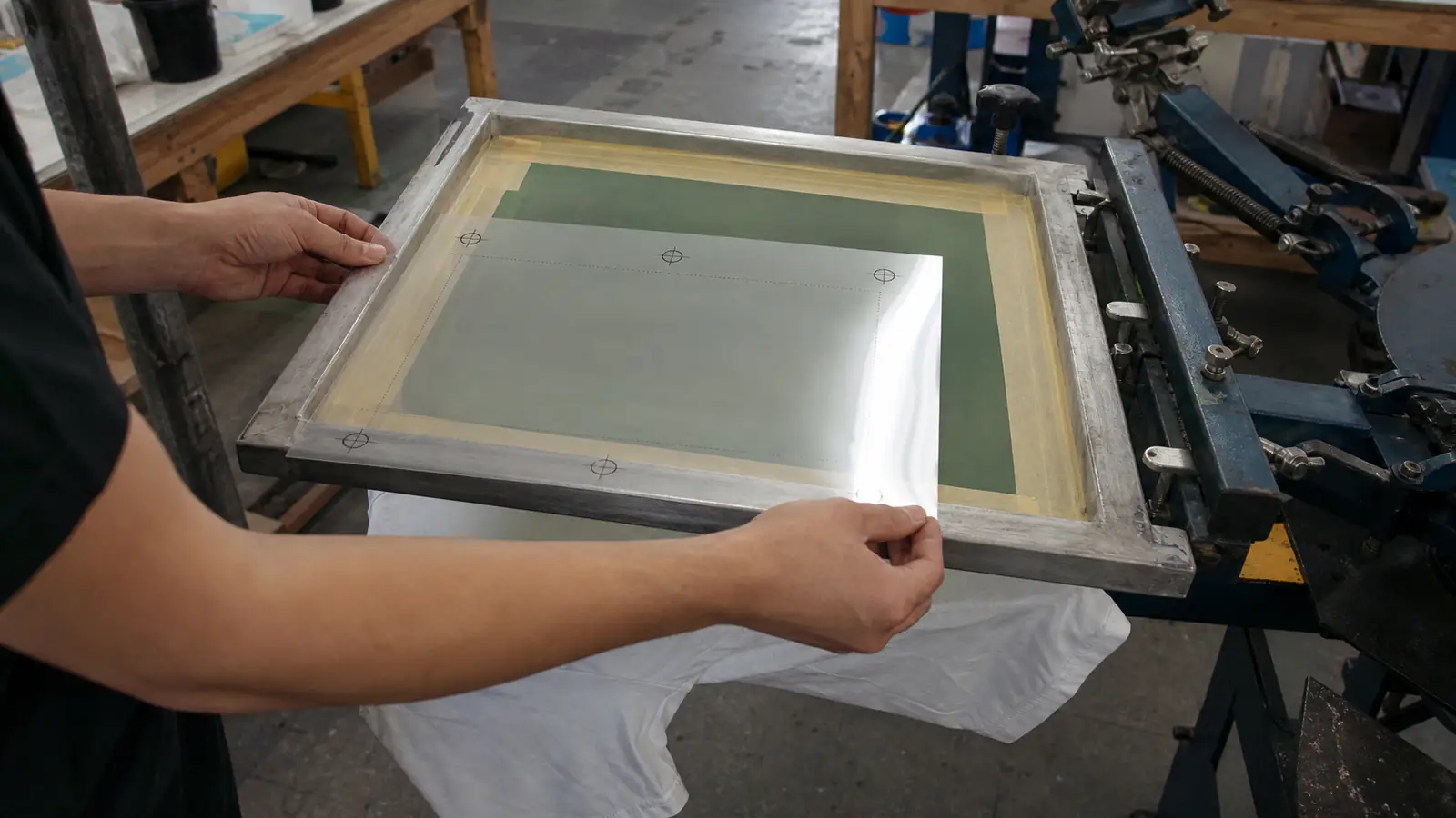 Print operator aligning registration marks over a prepared mesh screen