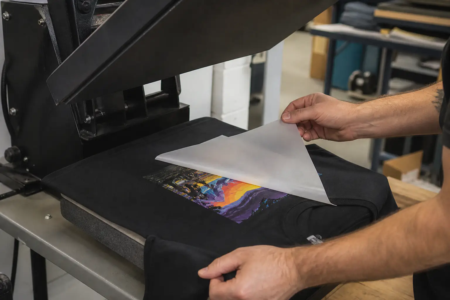 Print operator peeling the frosted carrier film from a DTF transfer on an open heat press