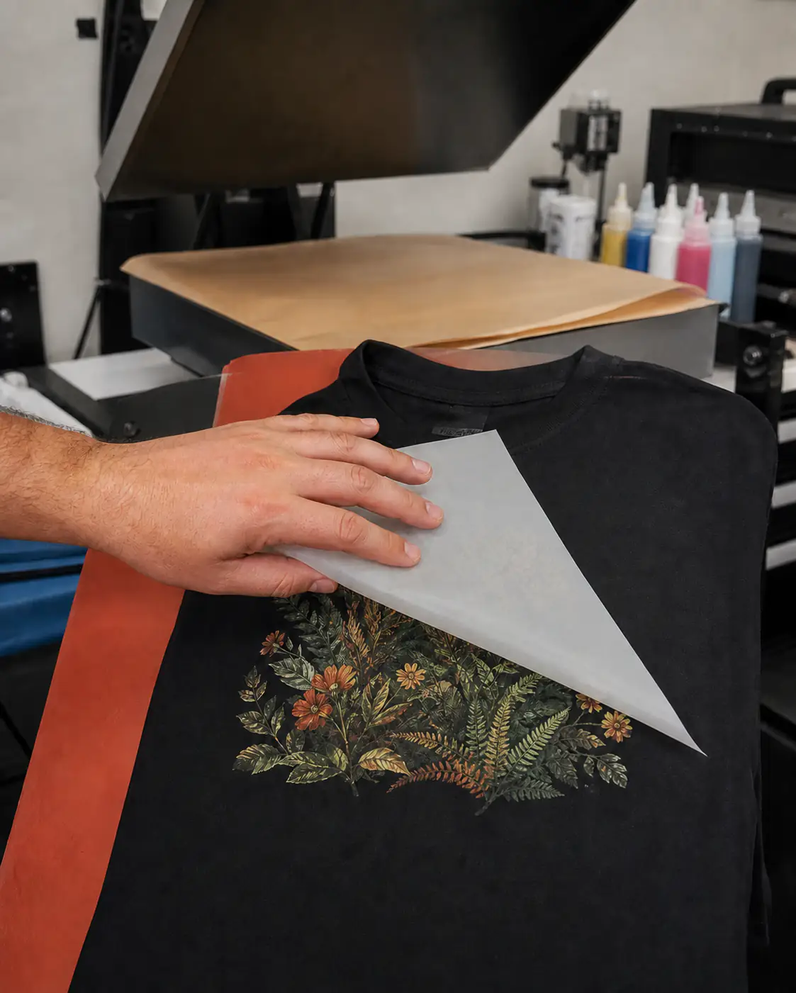 Print operator peeling a lightly translucent frosted carrier from a botanical DTF print